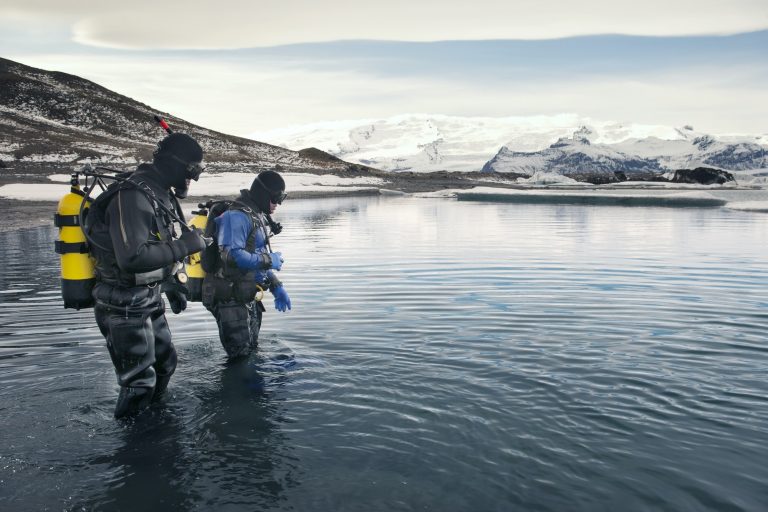 Scuba Divers Standing In Sea Against Cloudy Sky